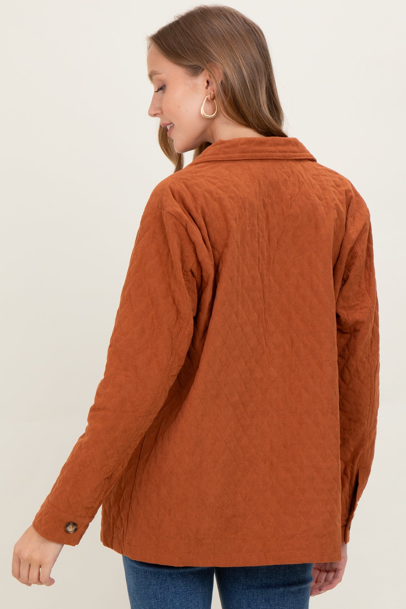 woman wearing a rust quilted maternity jacket with a collar and buttoned cuffs, showing a relaxed fit from the back