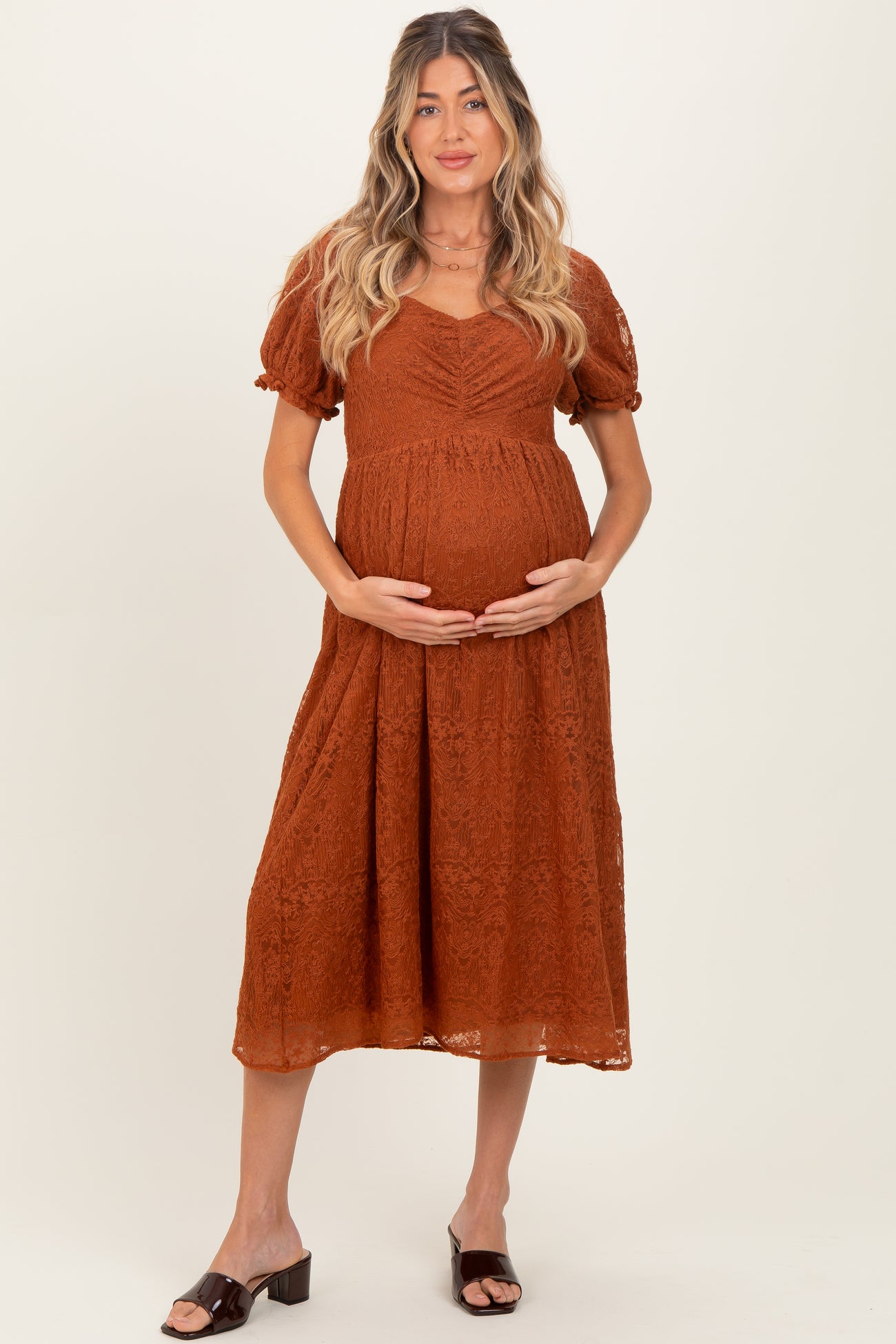 woman wearing an orange lace maternity dress and holding her baby bump
