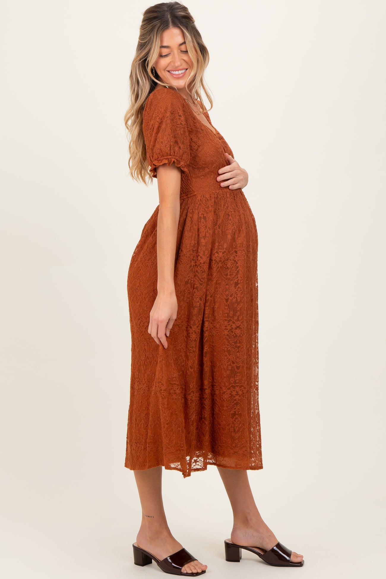 woman wearing a rust colored lace maternity dress with short puff sleeves and a visible baby bump
