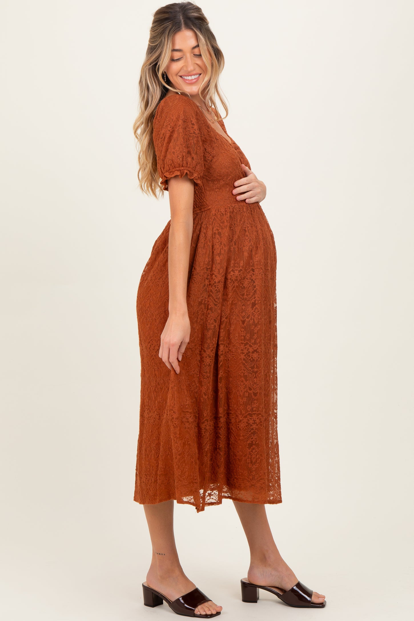 woman wearing a rust colored lace maternity dress with short puff sleeves and a visible baby bump