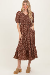 woman wearing a brown floral midi dress with puff sleeves and a tiered hem, posing with hands on her hips