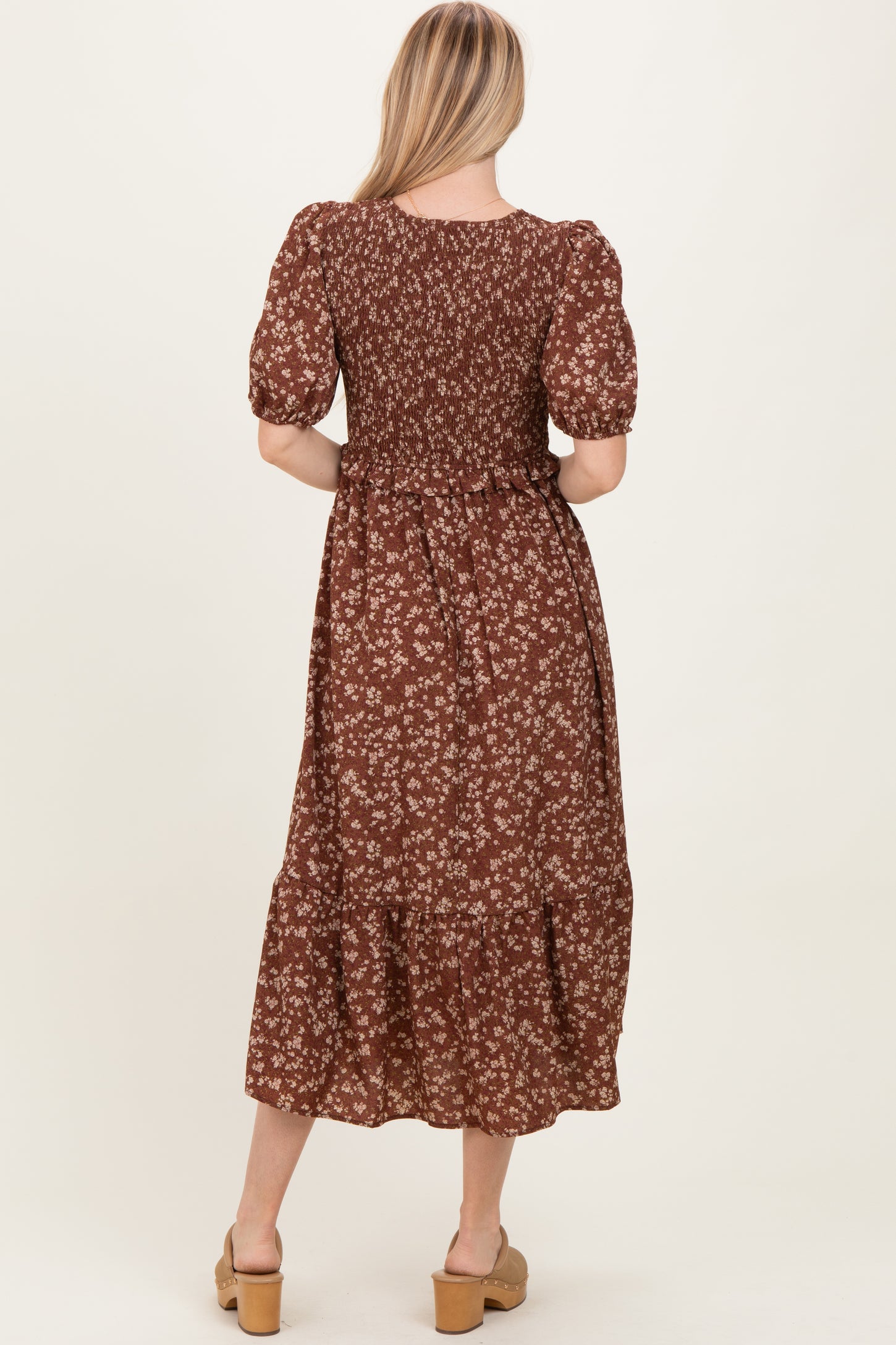woman wearing a brown floral midi dress with puff sleeves and a tiered hem, showing the back view