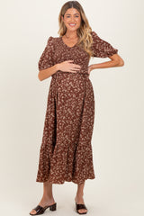 woman wearing a brown floral maternity dress with puff sleeves and a tiered skirt, holding her baby bump