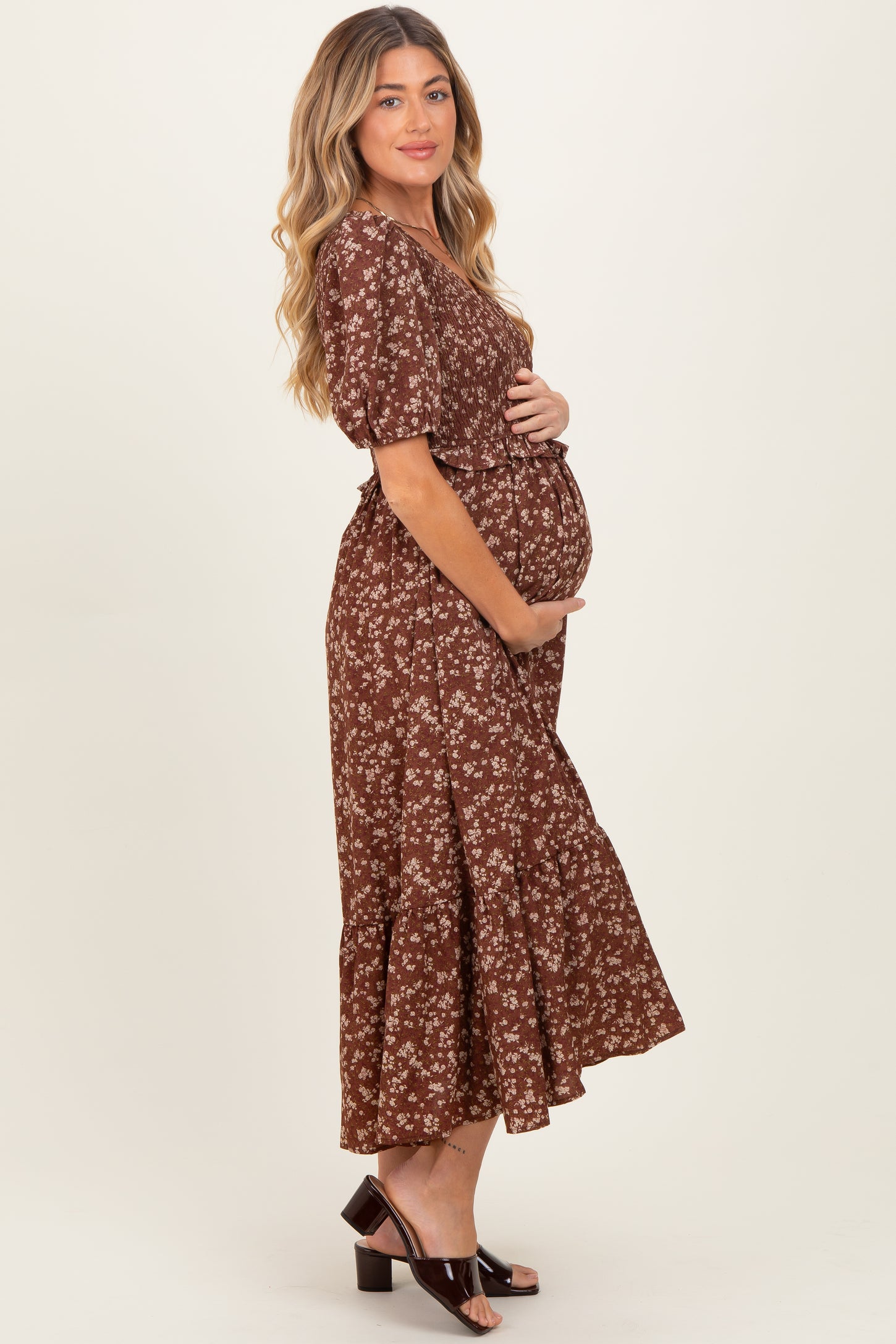 woman wearing a brown floral maternity dress with a ruffled hemline and holding her baby bump