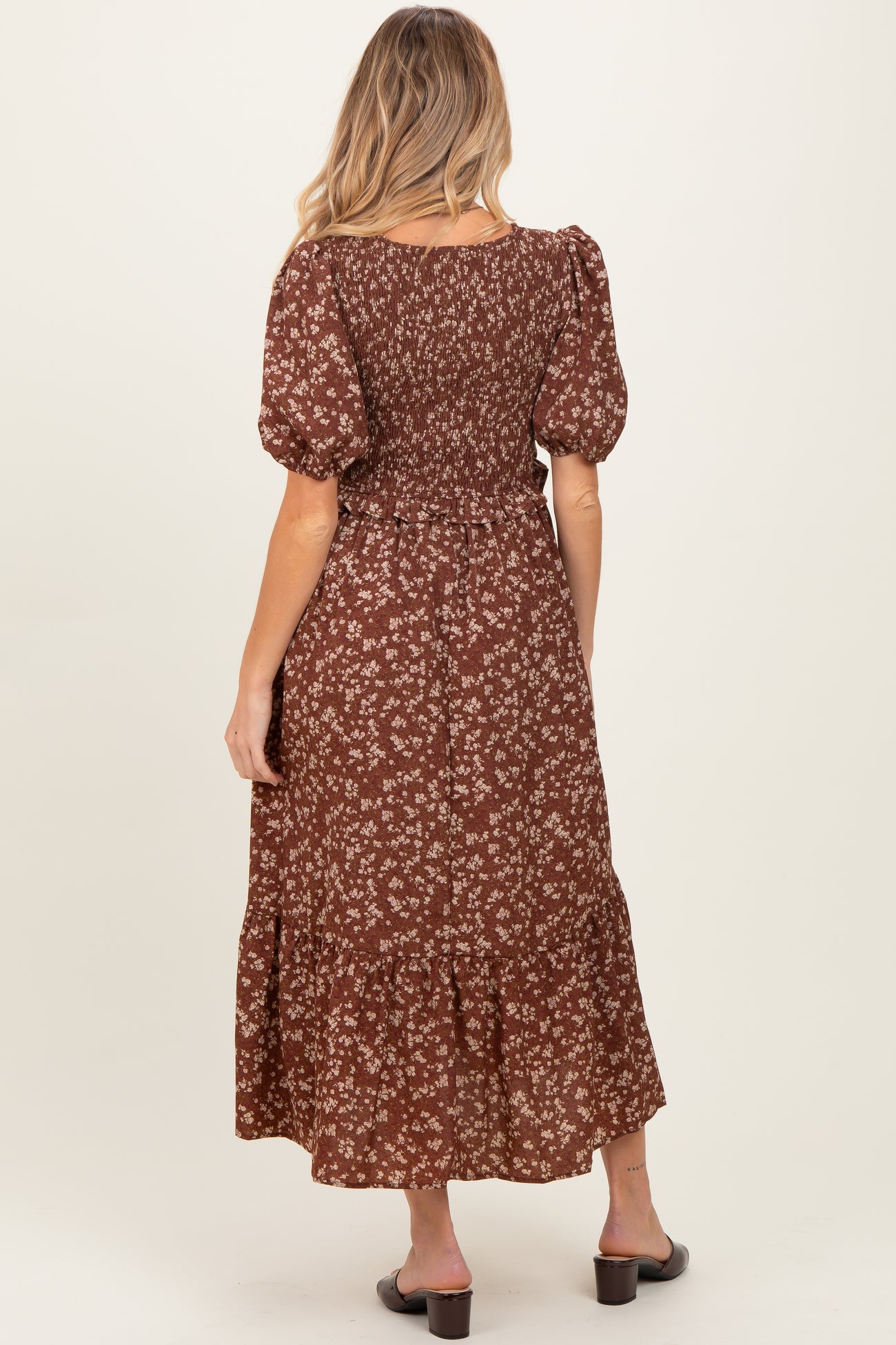 woman wearing a brown floral maternity dress with puff sleeves and a tiered skirt, showing a baby bump from the back