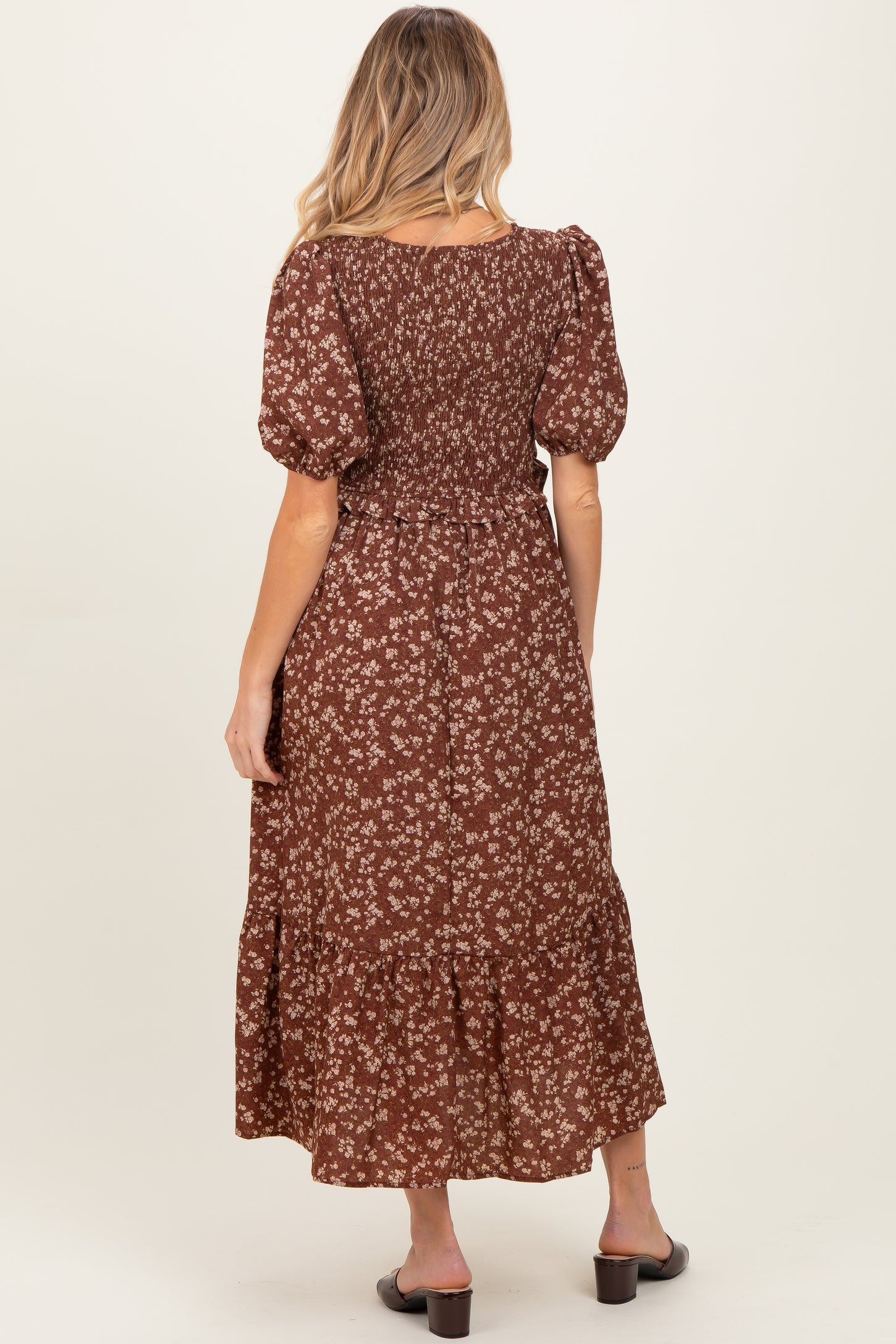 woman wearing a brown floral maternity dress with puff sleeves and a tiered skirt, showing a baby bump from the back