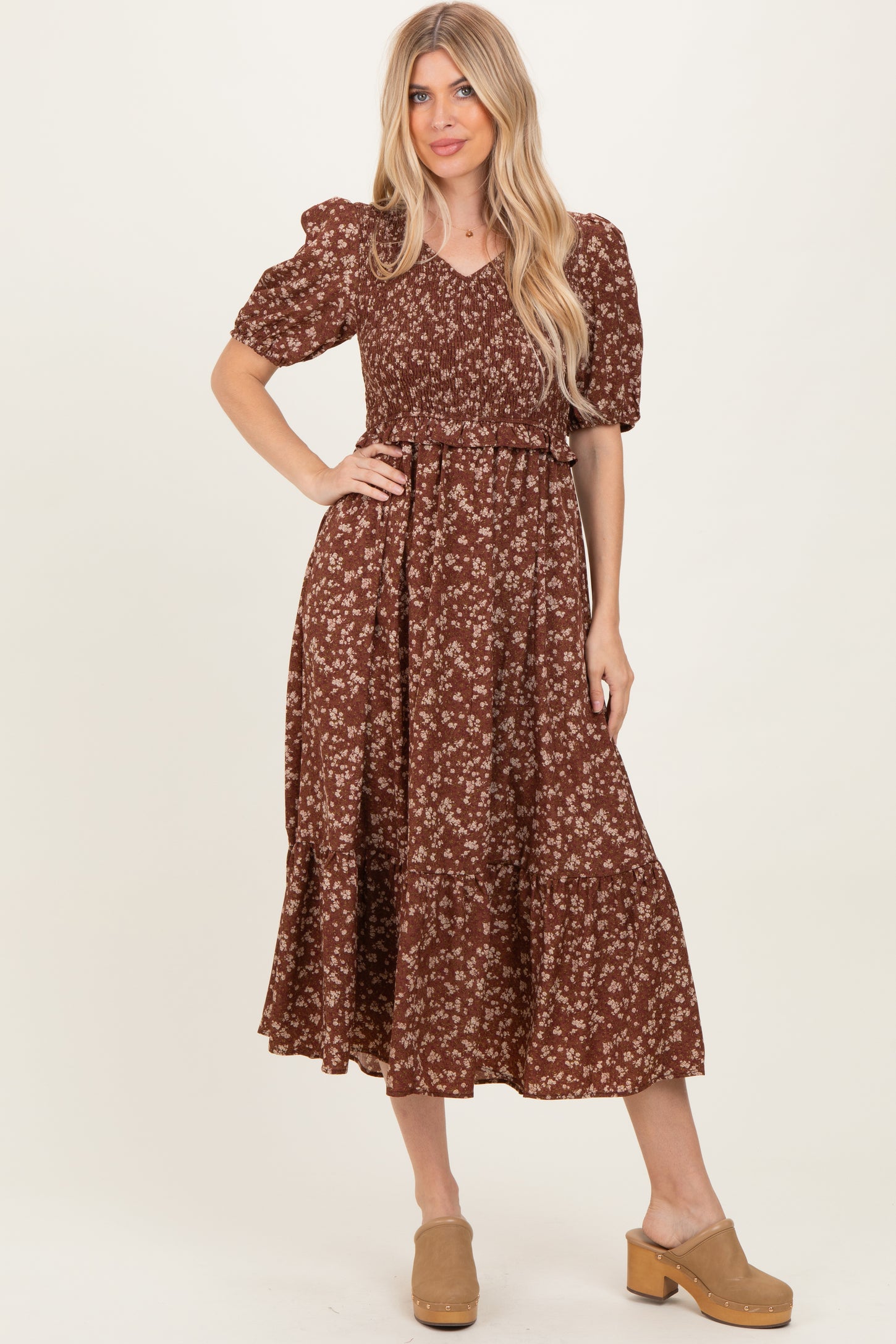woman wearing a brown floral print midi dress with puff sleeves and a tiered skirt, posing with one hand on her hip