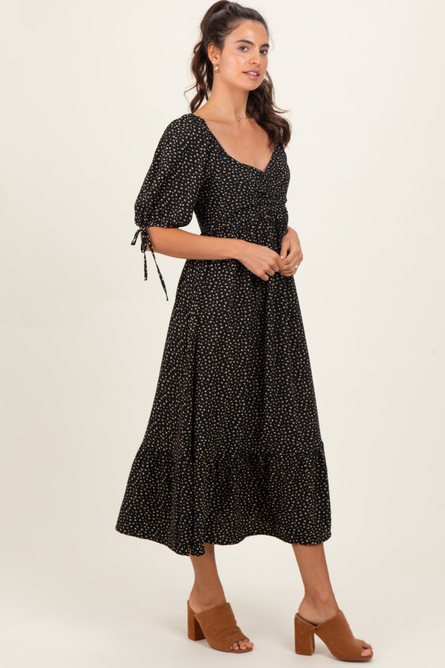 woman wearing a black midi dress with puff sleeves and gold polka dots, styled with brown heeled sandals