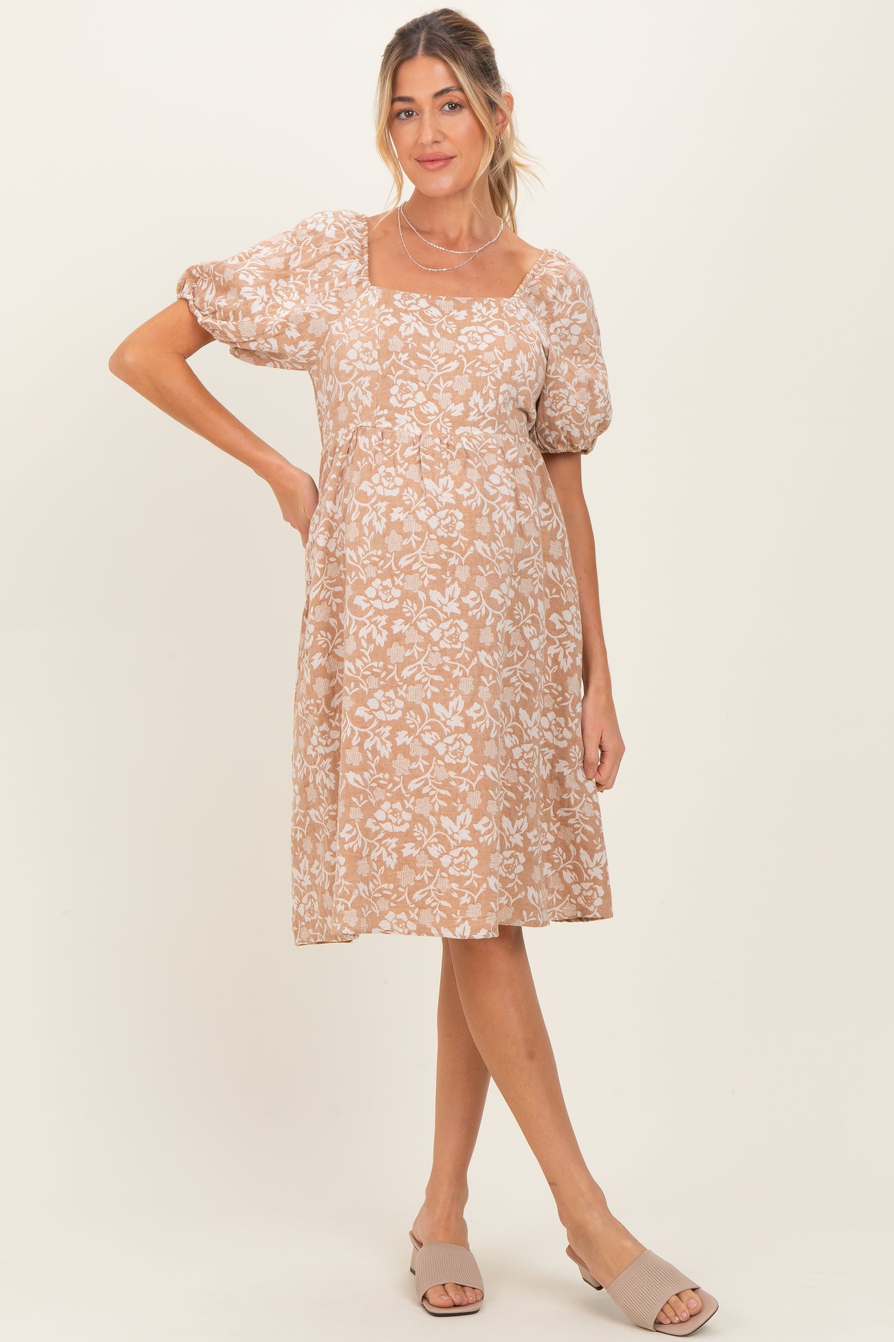 woman wearing a beige floral maternity dress with puff sleeves and a square neckline, showcasing her baby bump