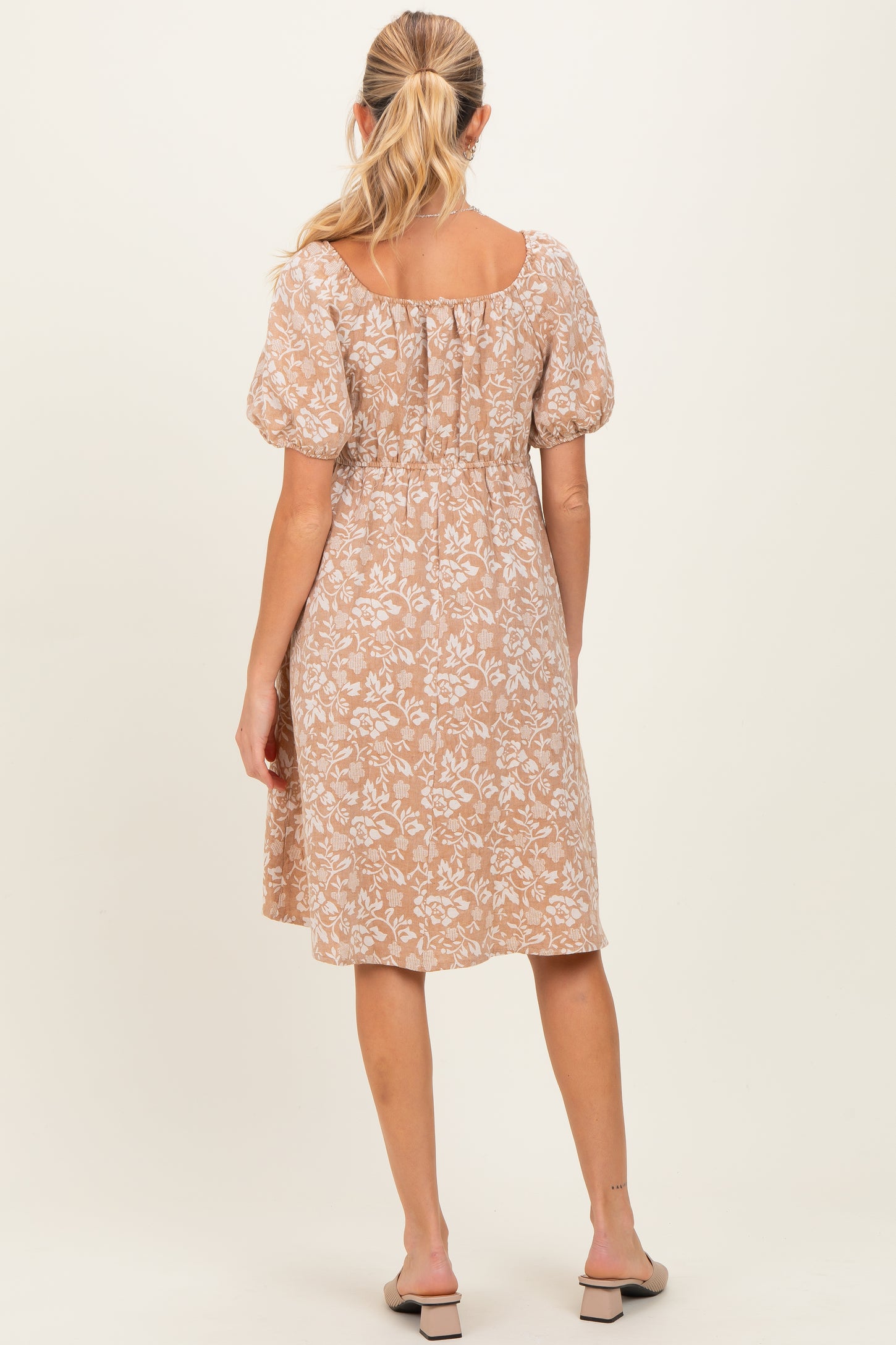 woman wearing a floral print beige maternity dress with a smocked back and puff sleeves