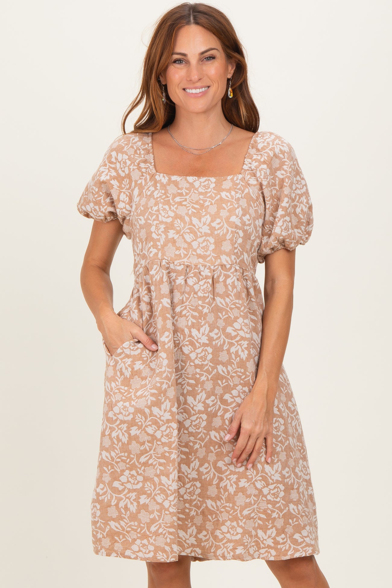 woman wearing a beige floral print puff sleeve dress with a square neckline and pockets