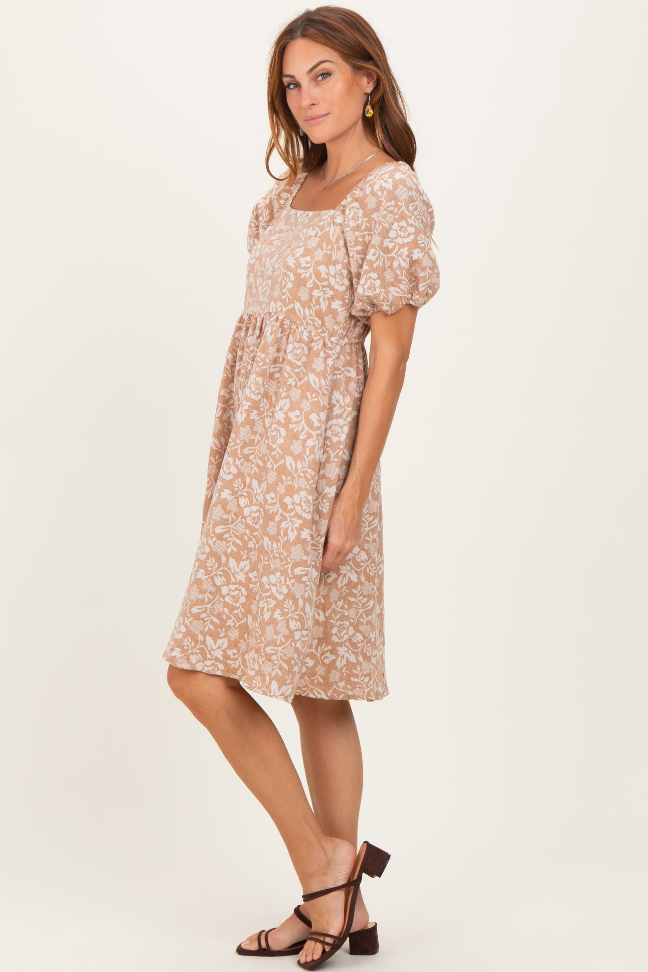 woman wearing a tan floral print puff sleeve dress and strappy brown sandals