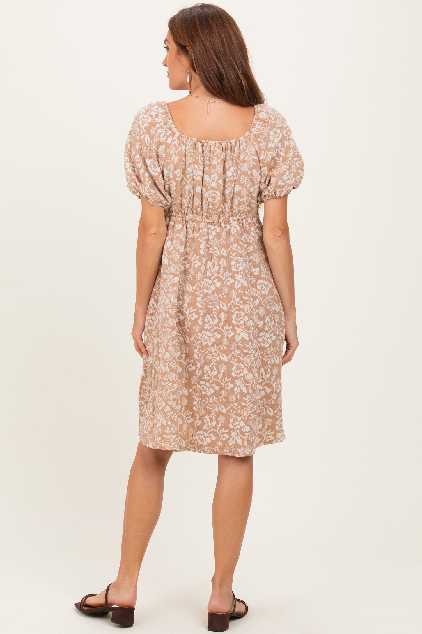 woman wearing a beige floral print dress with puff sleeves and a smocked waist, viewed from the back