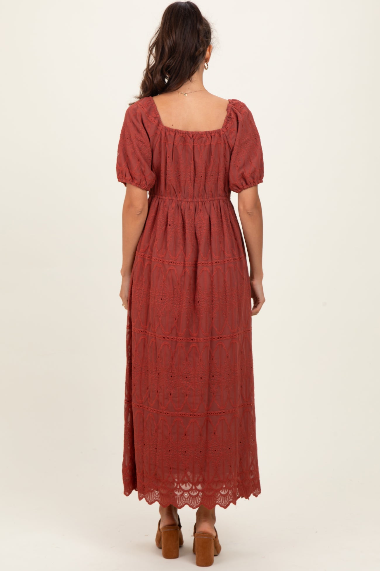 woman wearing a rust-colored maxi dress with puff sleeves and lace detailing, viewed from the back