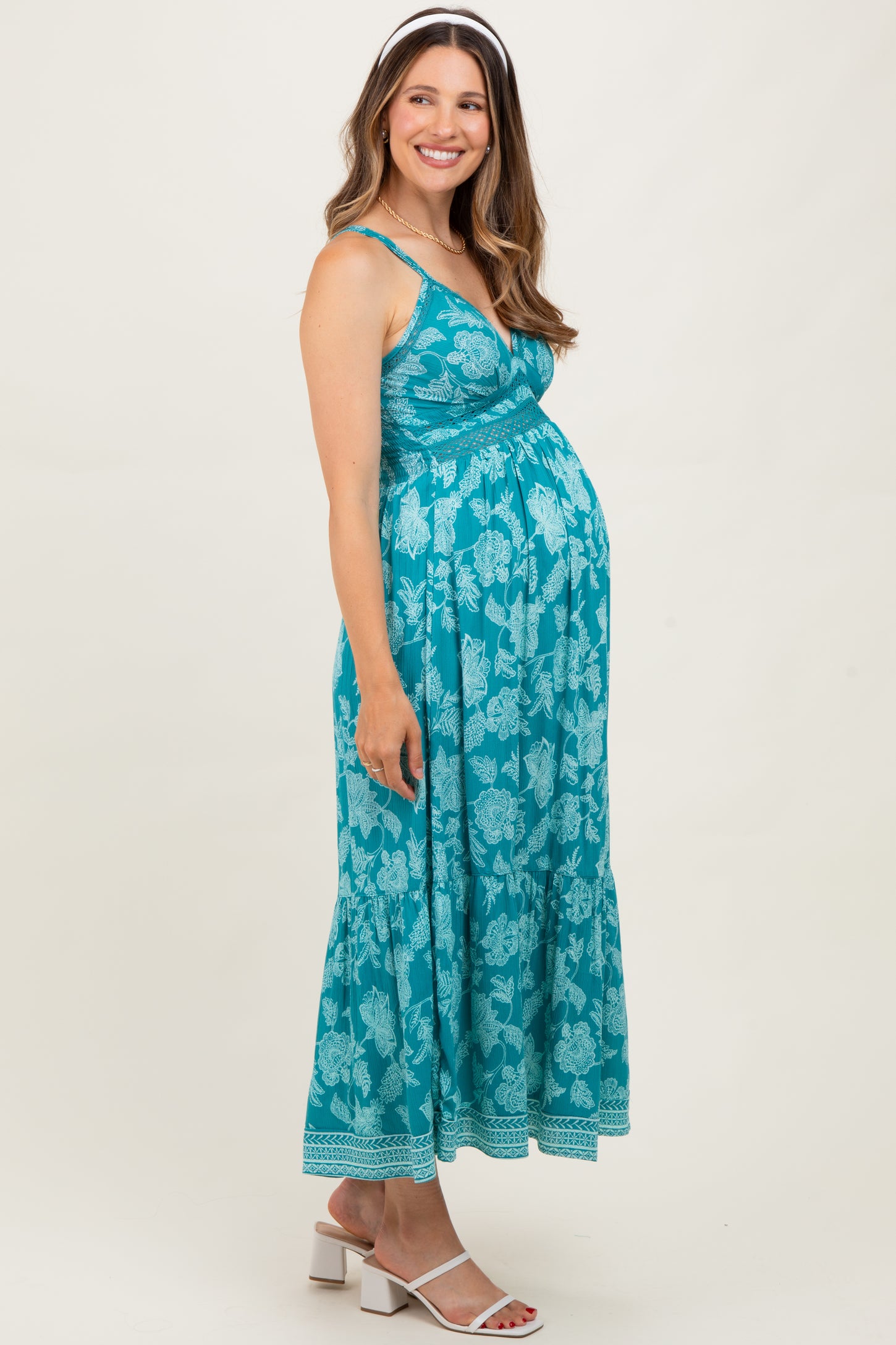woman wearing a teal floral maternity maxi dress with a fitted bodice and flowy skirt, showing her baby bump