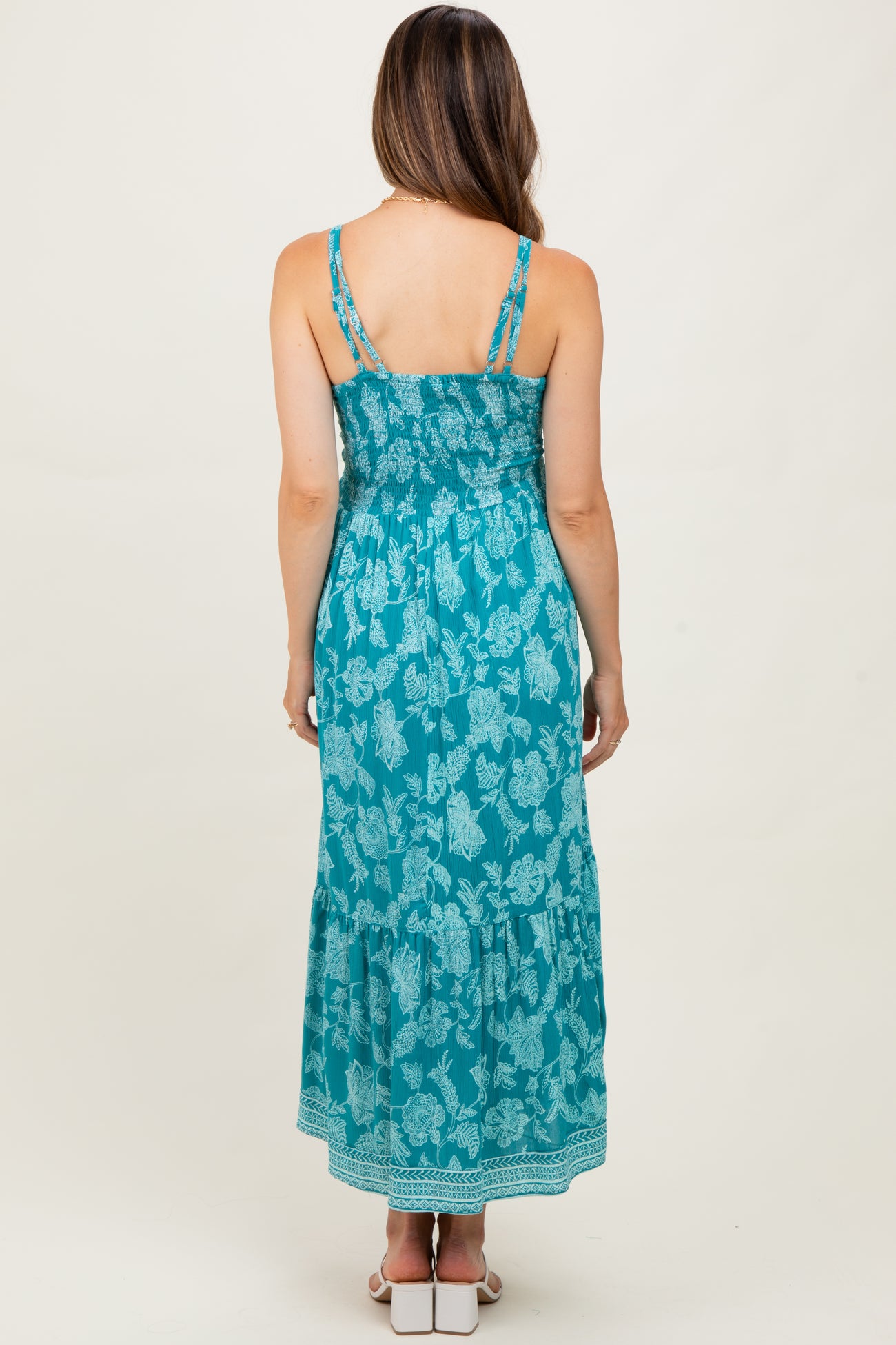 woman wearing a turquoise floral print maternity maxi dress with adjustable straps and a ruffled hem