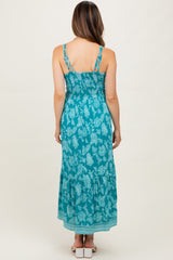 woman wearing a turquoise floral print maternity maxi dress with adjustable straps and a ruffled hem