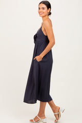 woman wearing a navy blue sleeveless midi dress with a tie detail and pockets, standing sideways on a light background