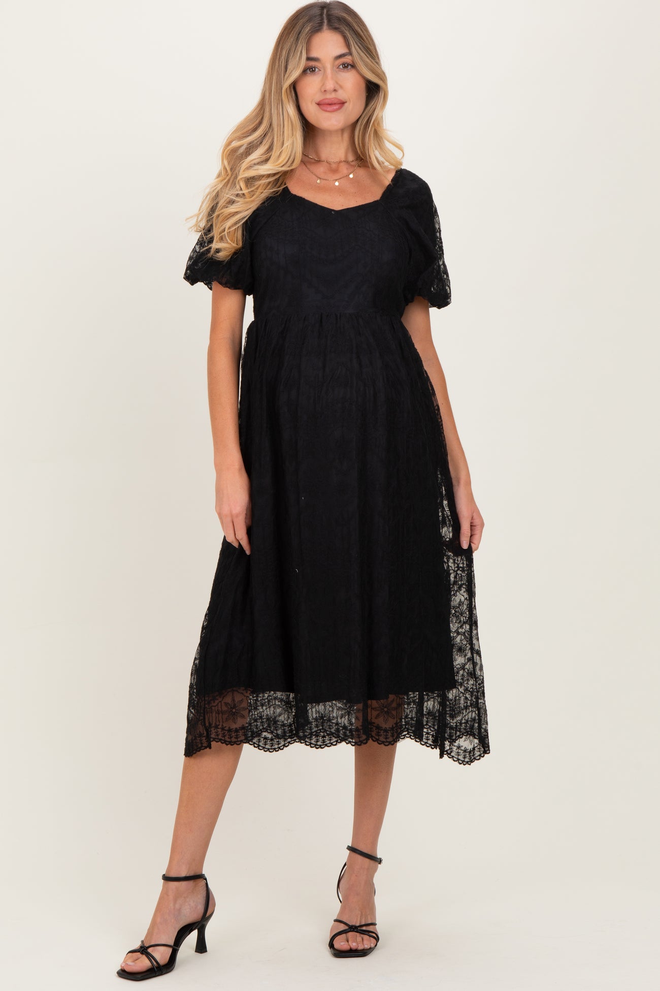 woman wearing a black lace maternity dress with short puff sleeves and a flowing skirt, showing a baby bump