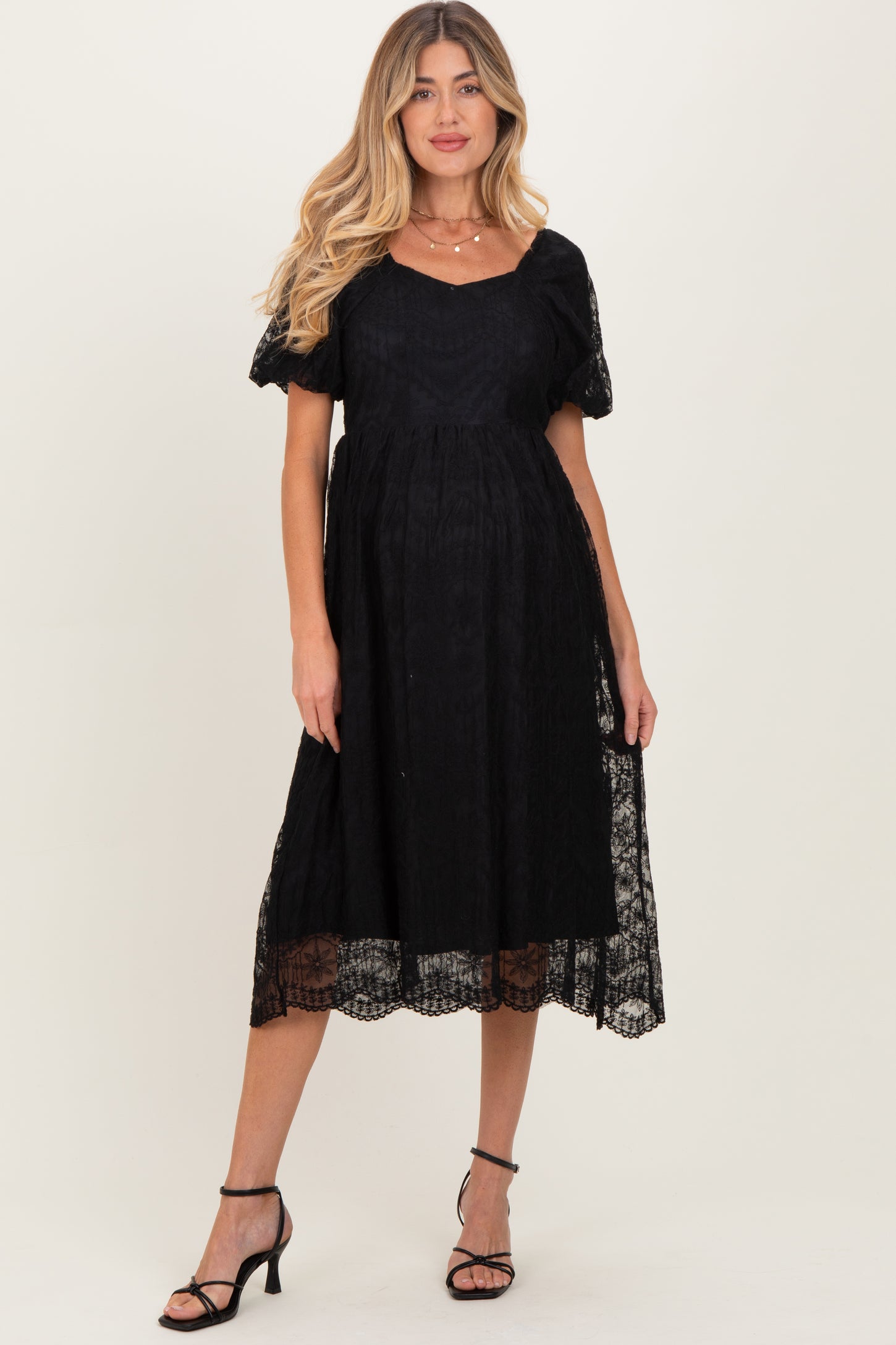 woman wearing a black lace maternity dress with short puff sleeves and a flowing skirt, showing a baby bump