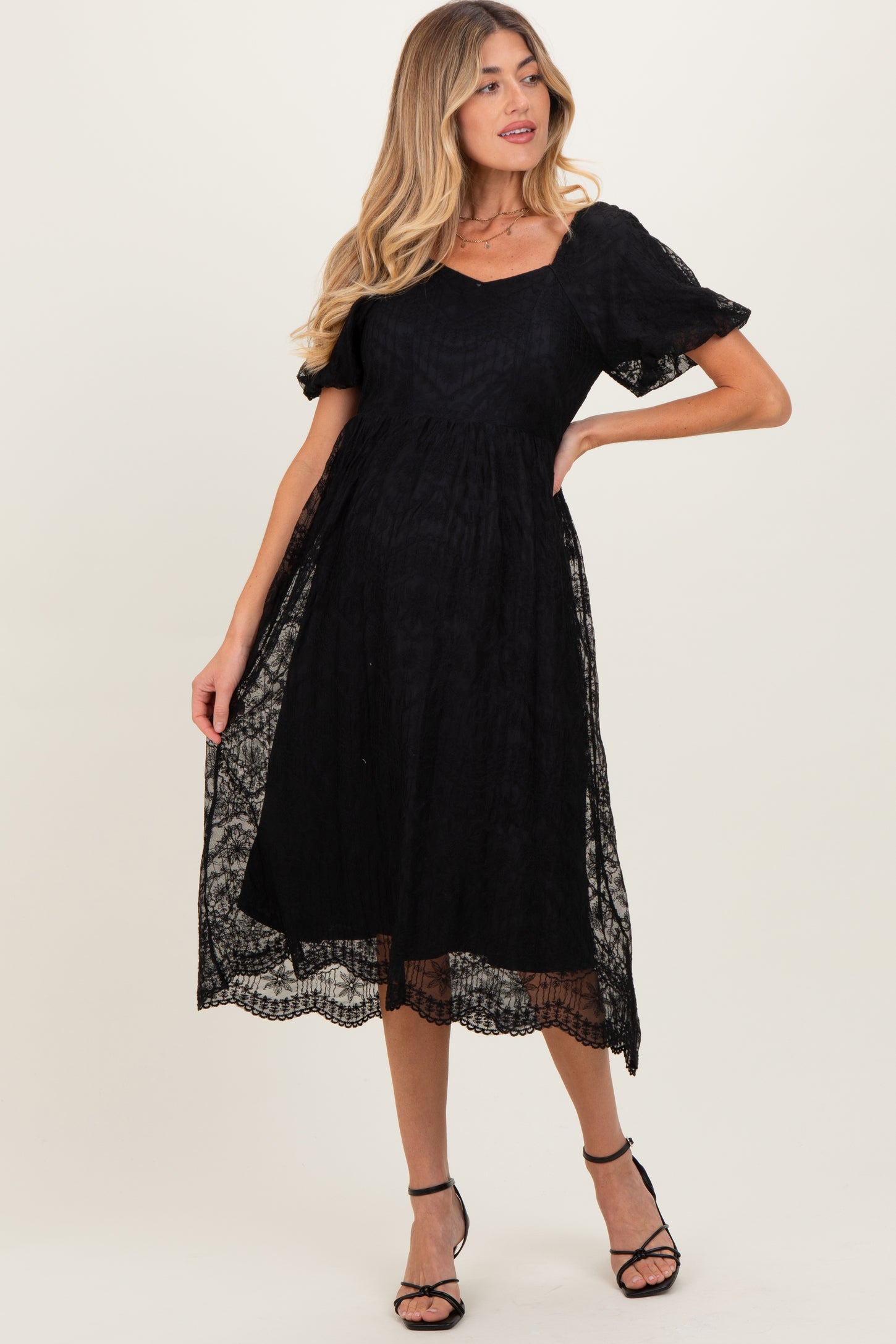 woman wearing a black lace maternity dress with short puff sleeves and a flowing skirt, showcasing her baby bump