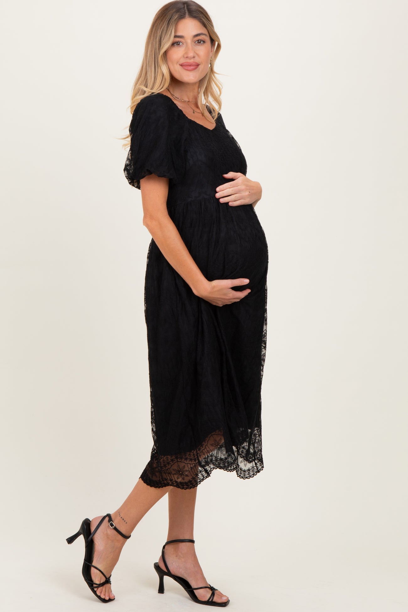 woman wearing a black lace maternity dress with short sleeves and holding her baby bump