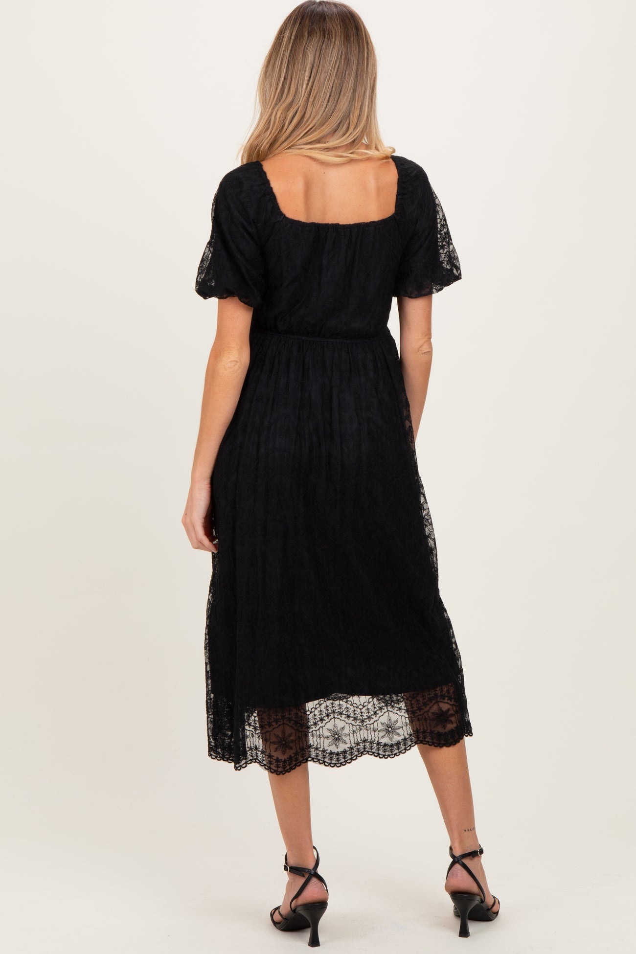 woman wearing a black lace maternity dress with short puff sleeves and a square neckline, showing a flowing skirt
