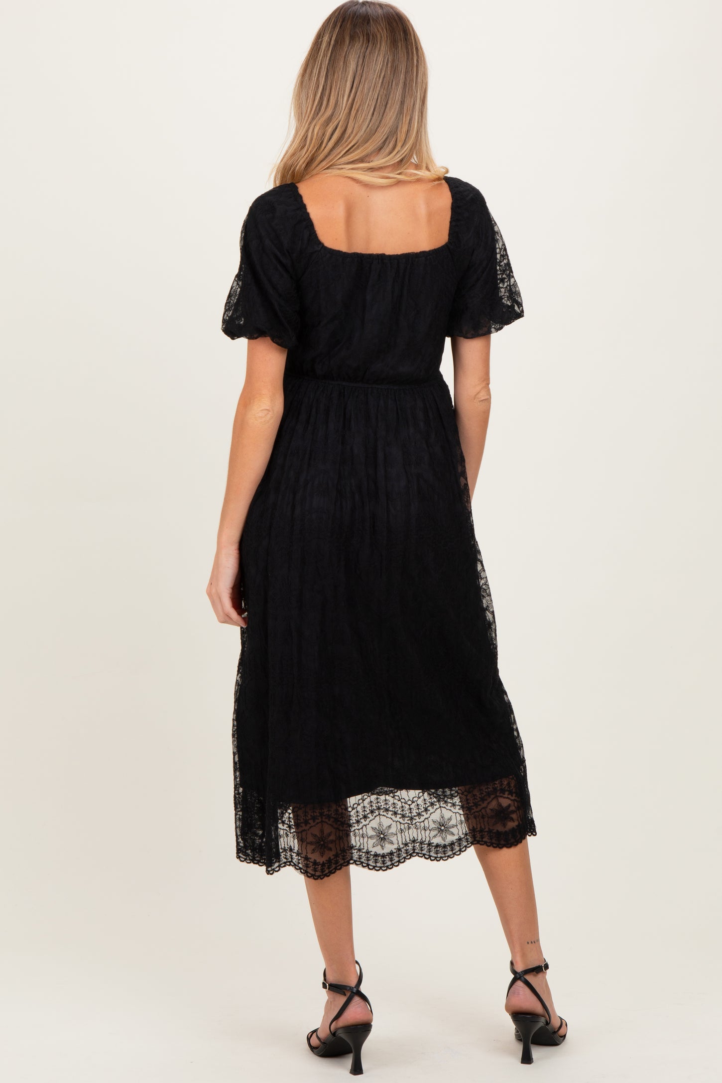 woman wearing a black lace maternity dress with short puff sleeves and a square neckline, showing a flowing skirt