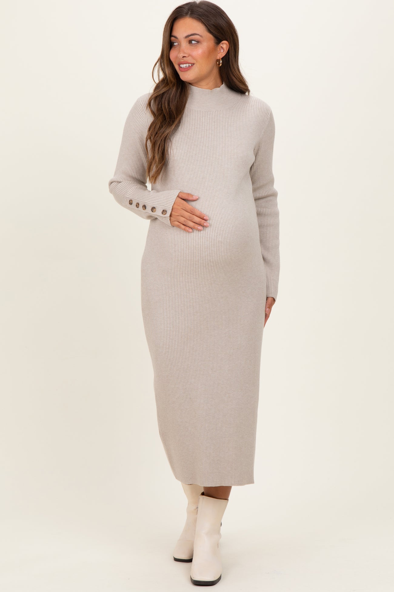 woman wearing a beige ribbed maternity dress with long sleeves and button details, holding her baby bump