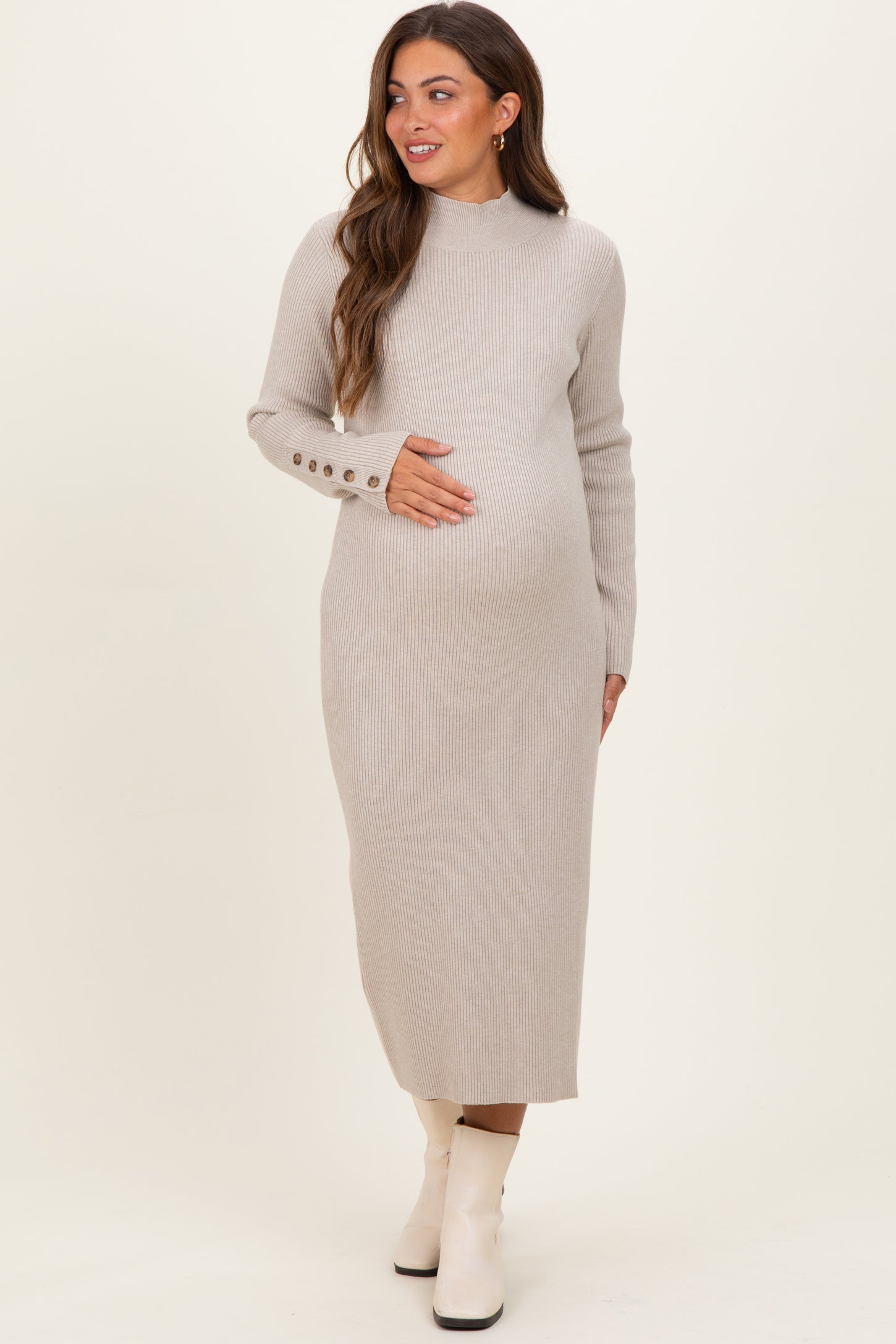 woman wearing a beige ribbed maternity dress with long sleeves and button details, holding her baby bump
