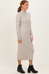 woman wearing a beige ribbed knit long sleeve dress with button details on the sleeves and black ankle boots