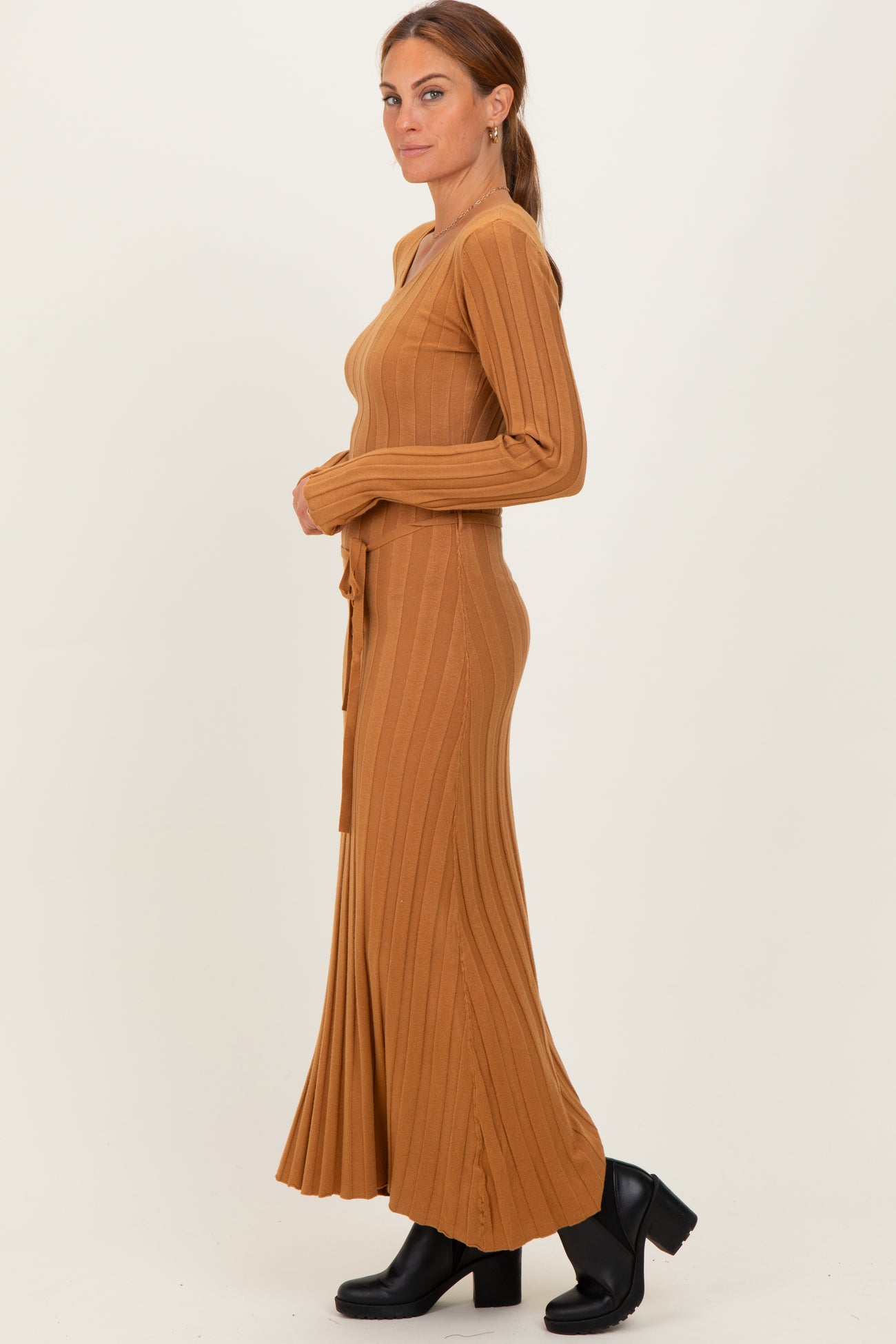 woman wearing a brown ribbed long sleeve maxi dress with a tie waist and flared hem, styled with black heeled boots