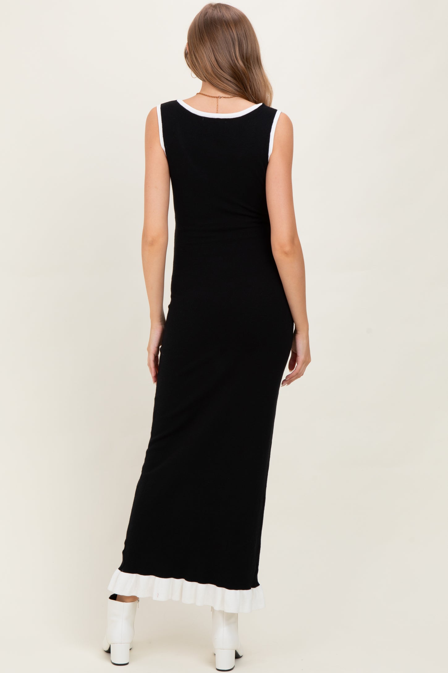 woman wearing a black maternity maxi dress with a white ruffled hem and a sleeveless design, showing no baby bump