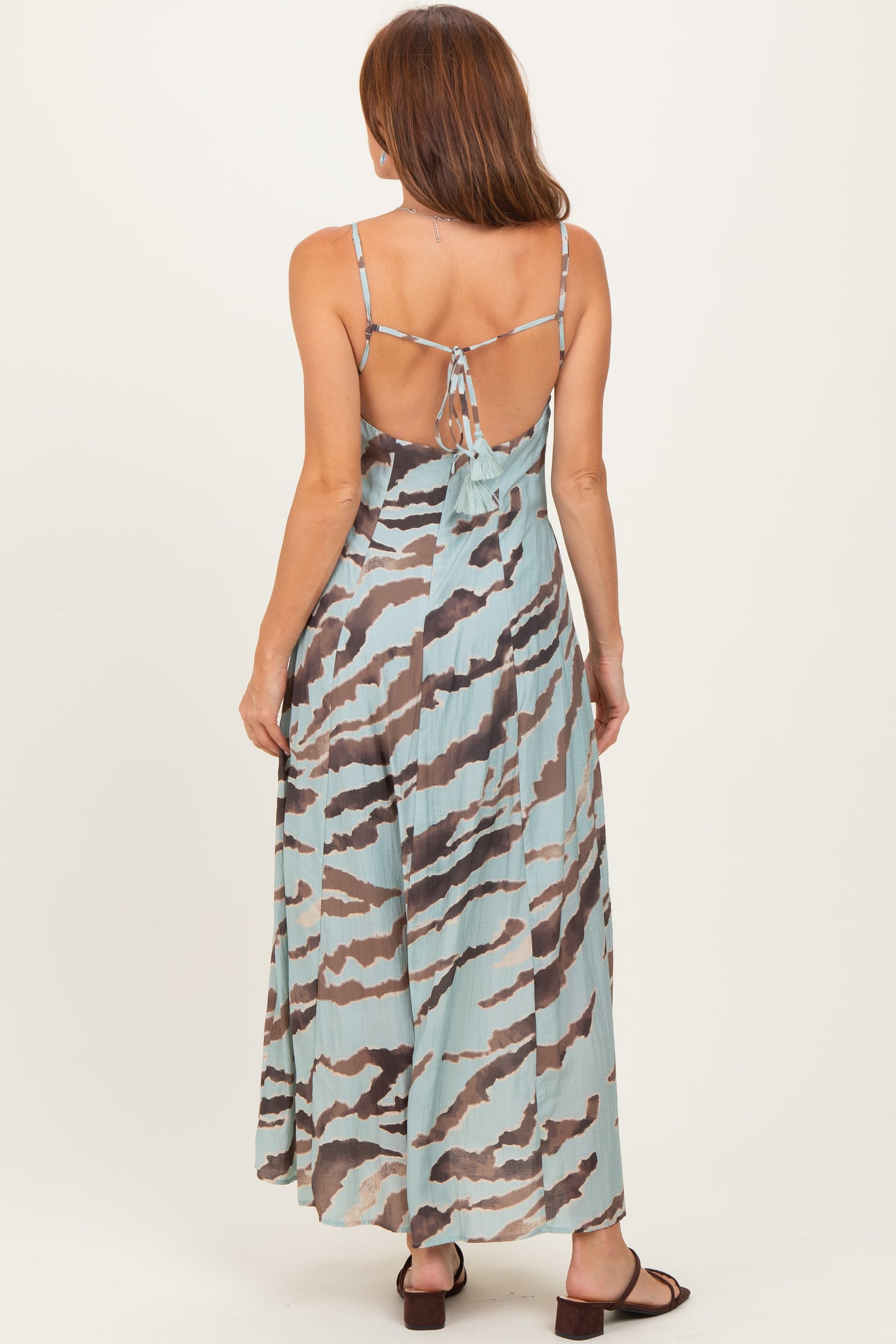 woman wearing a backless maxi dress with a light blue and brown abstract print, showing adjustable spaghetti straps