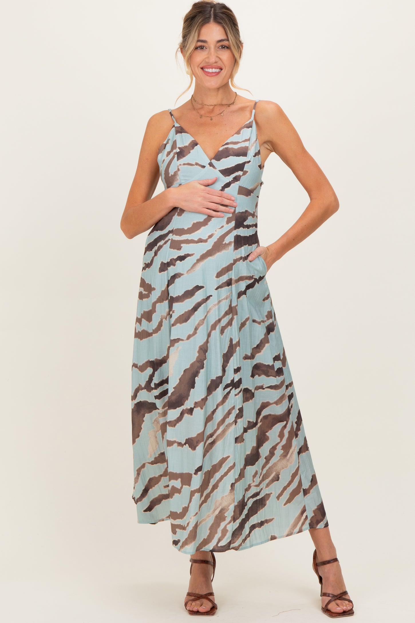 woman wearing a patterned maxi maternity dress in blue and brown, holding her baby bump with a smile