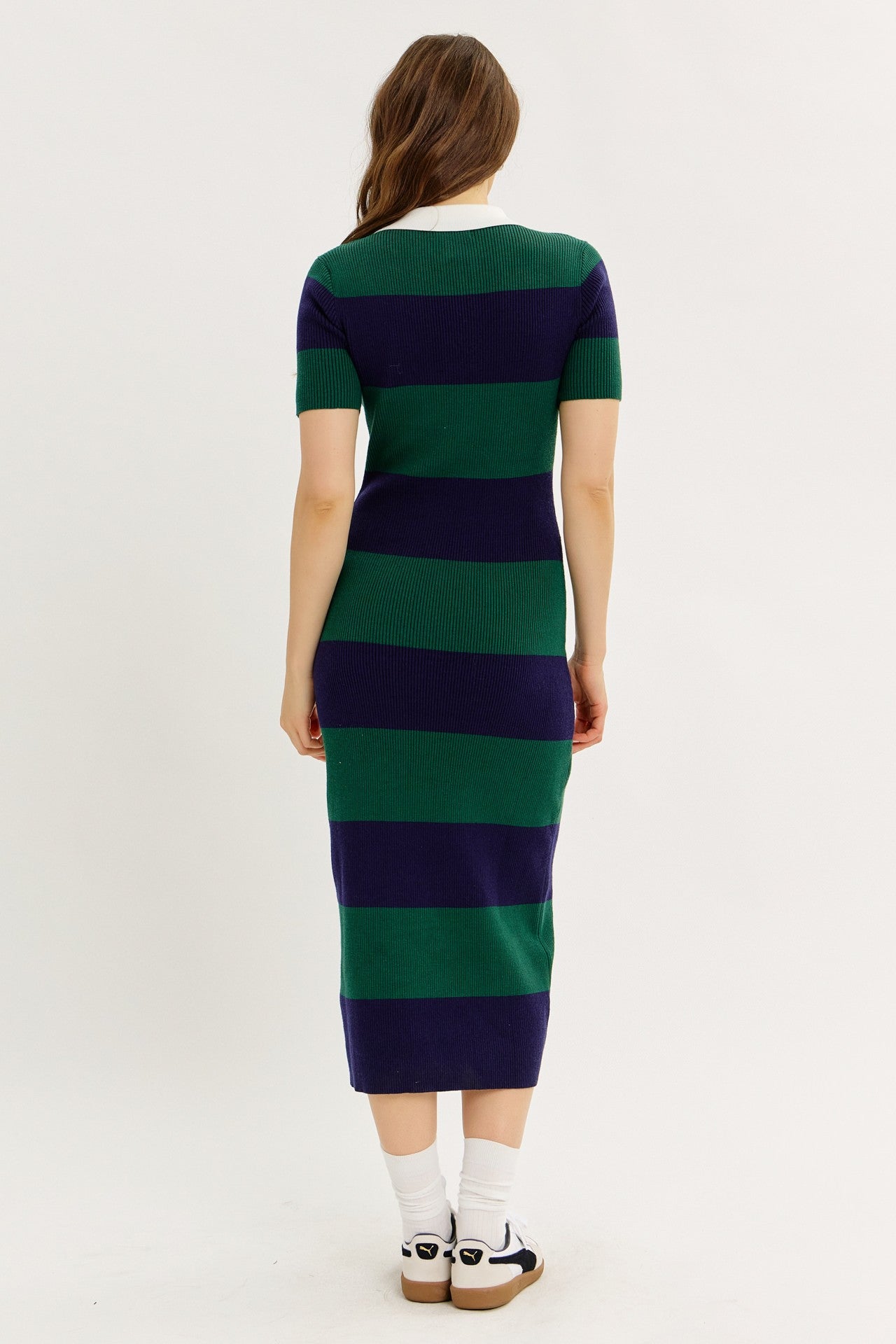 woman wearing a green and navy striped short sleeve midi dress, seen from the back, paired with white socks and sandals