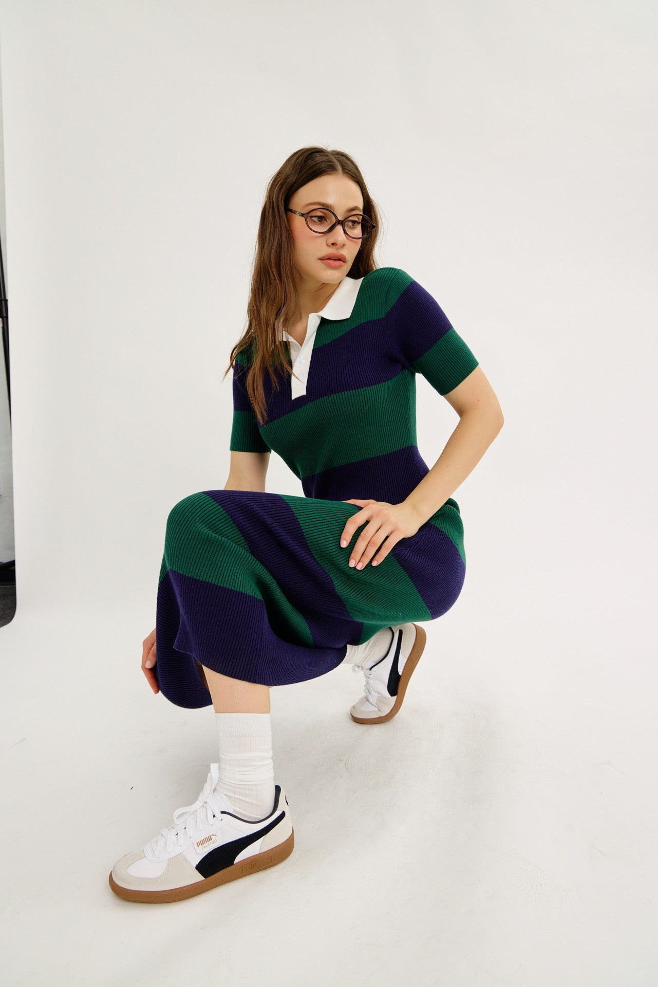 woman wearing a green and navy striped polo dress with short sleeves and white sneakers, crouching on the floor