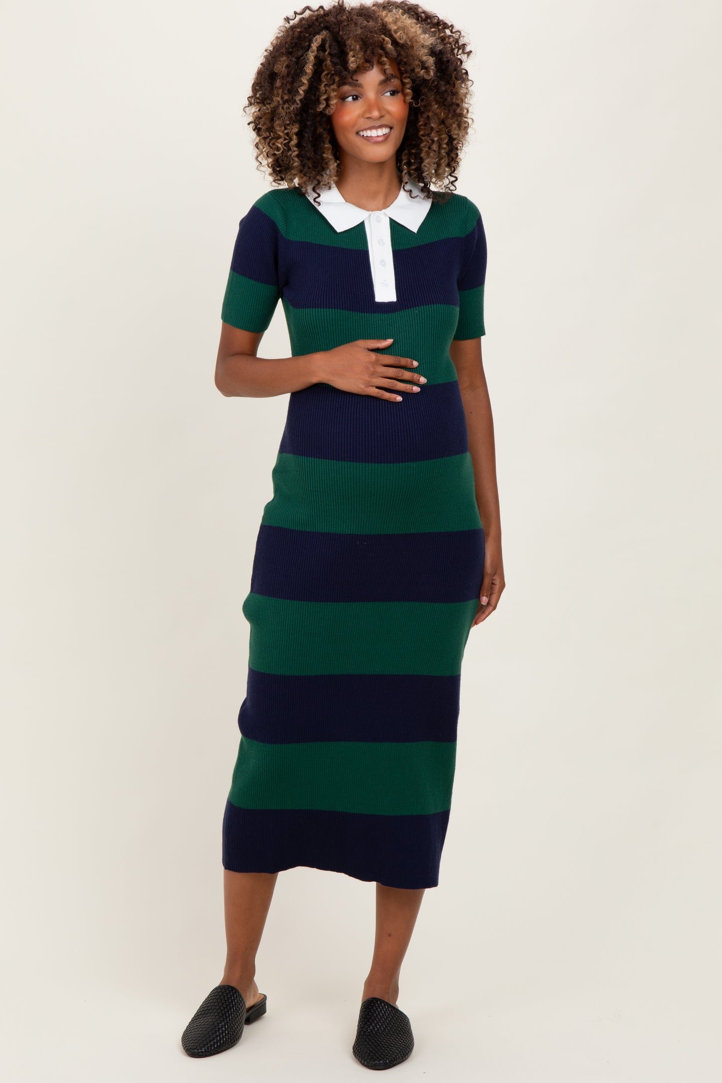 woman wearing a navy and green striped maternity dress with a white collar and holding her baby bump
