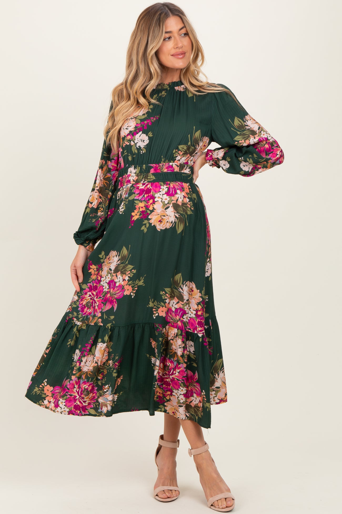 woman wearing a green floral maternity dress with long sleeves and a tiered skirt, showcasing her baby bump