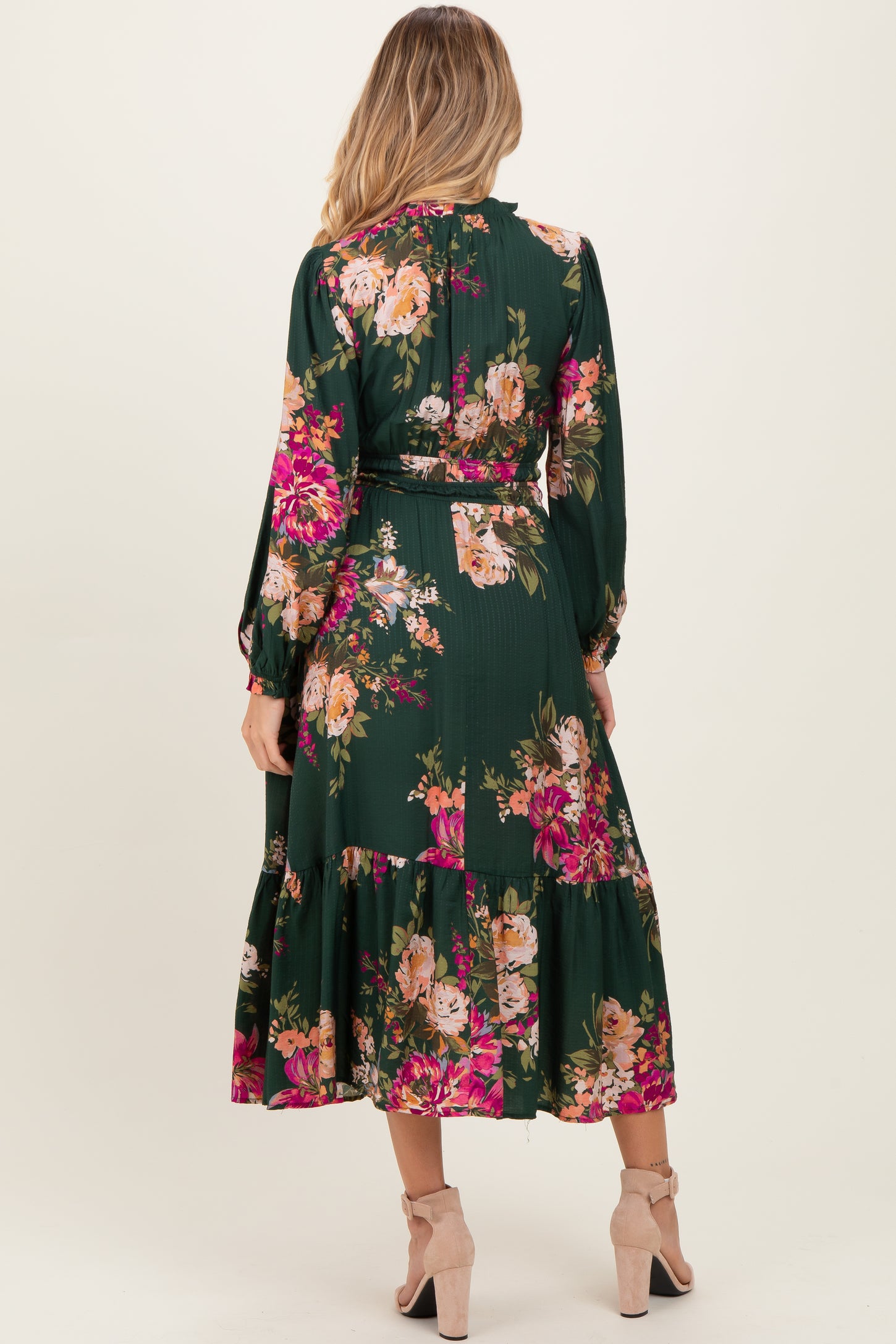 woman wearing a green floral maternity dress with long sleeves and a tiered skirt, showing a baby bump