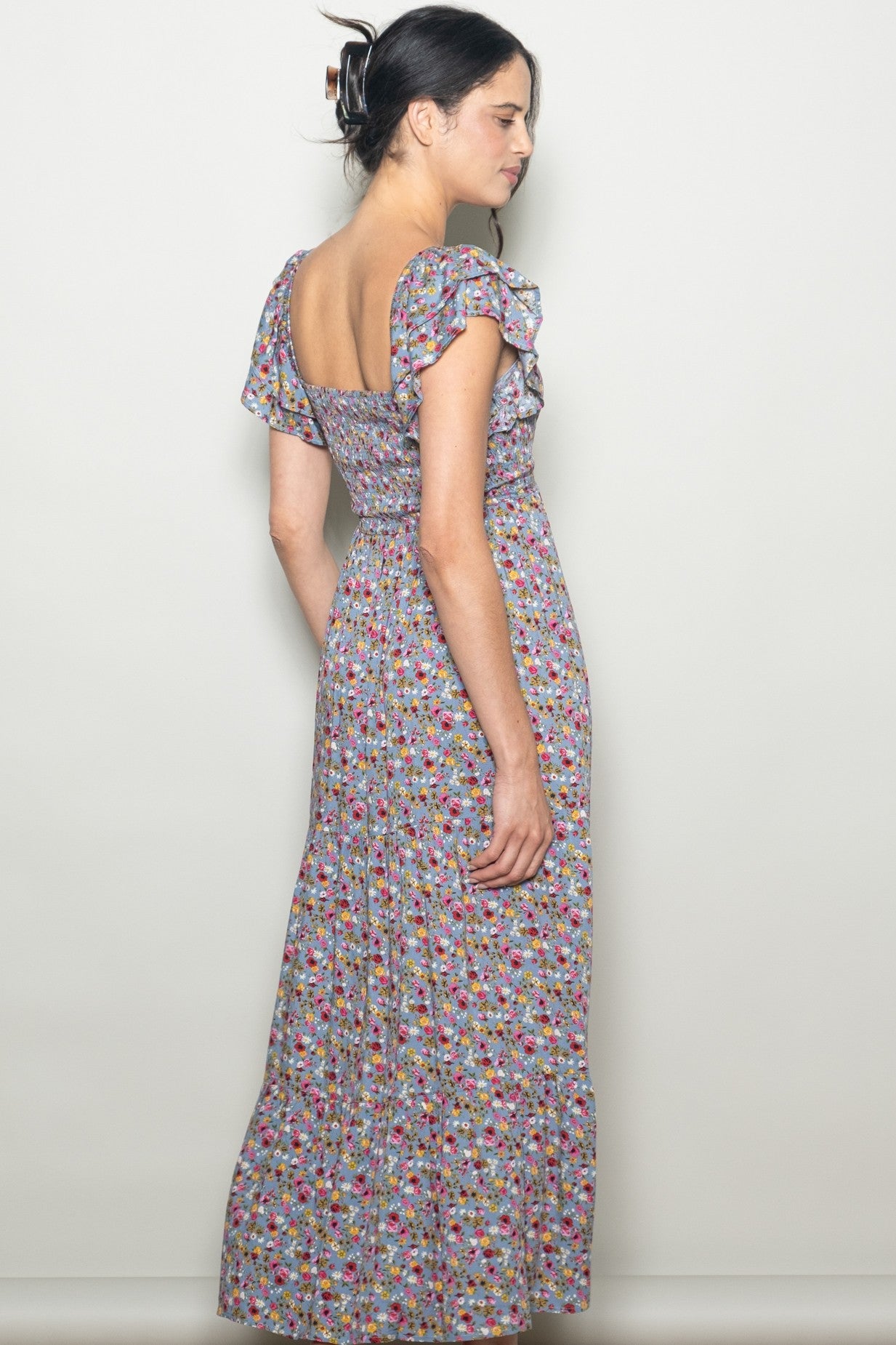 woman wearing a floral print maxi dress with short ruffled sleeves and a square back, shown from the side