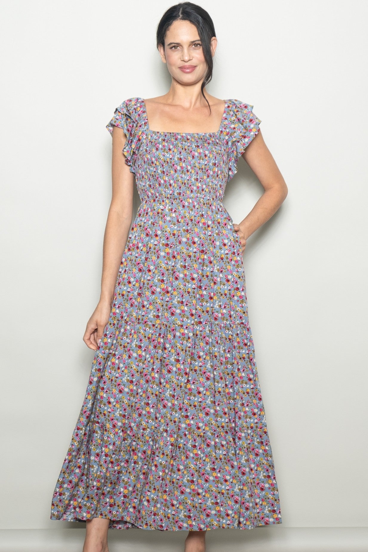 woman wearing a floral print maxi dress with cap sleeves and a smocked bodice, posing with one hand on her hip