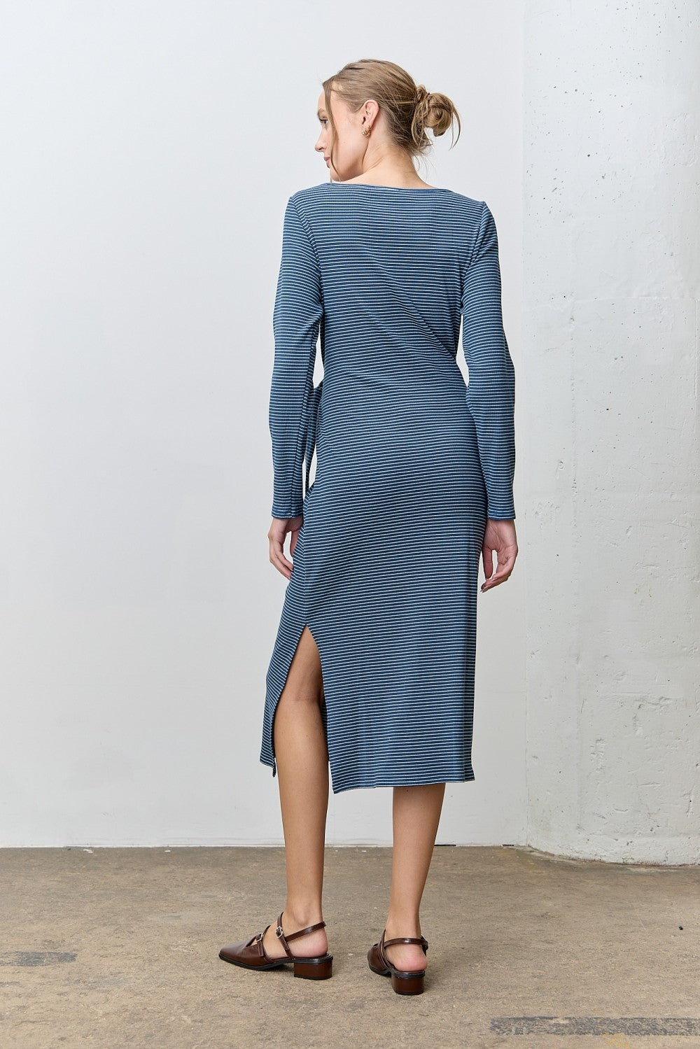 woman wearing a blue long sleeve midi dress with side slits, standing with her back to the camera