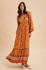 woman wearing a long sleeve bohemian floral maxi dress in orange and brown tones with a flowy skirt