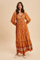 woman wearing an orange floral maxi dress with long sleeves and a tiered hem, styled with a v-neckline