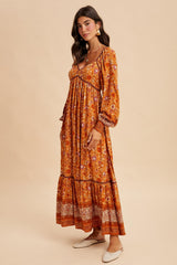 woman wearing a rust floral maxi dress with long sleeves and tiered hem, styled with flat shoes