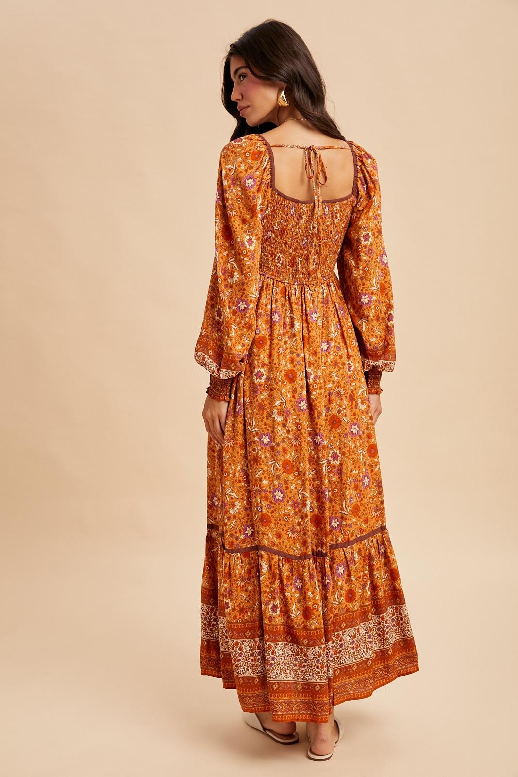 woman wearing a floral orange maxi dress with long sleeves and a tie-back detail, standing against a neutral background