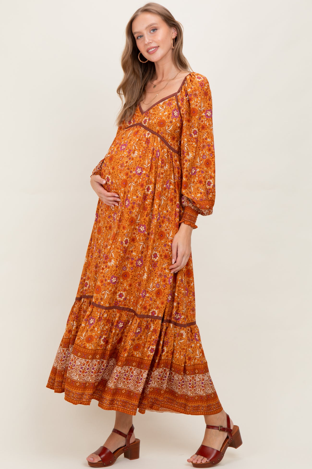woman wearing an orange floral maternity maxi dress with long sleeves and a baby bump visible