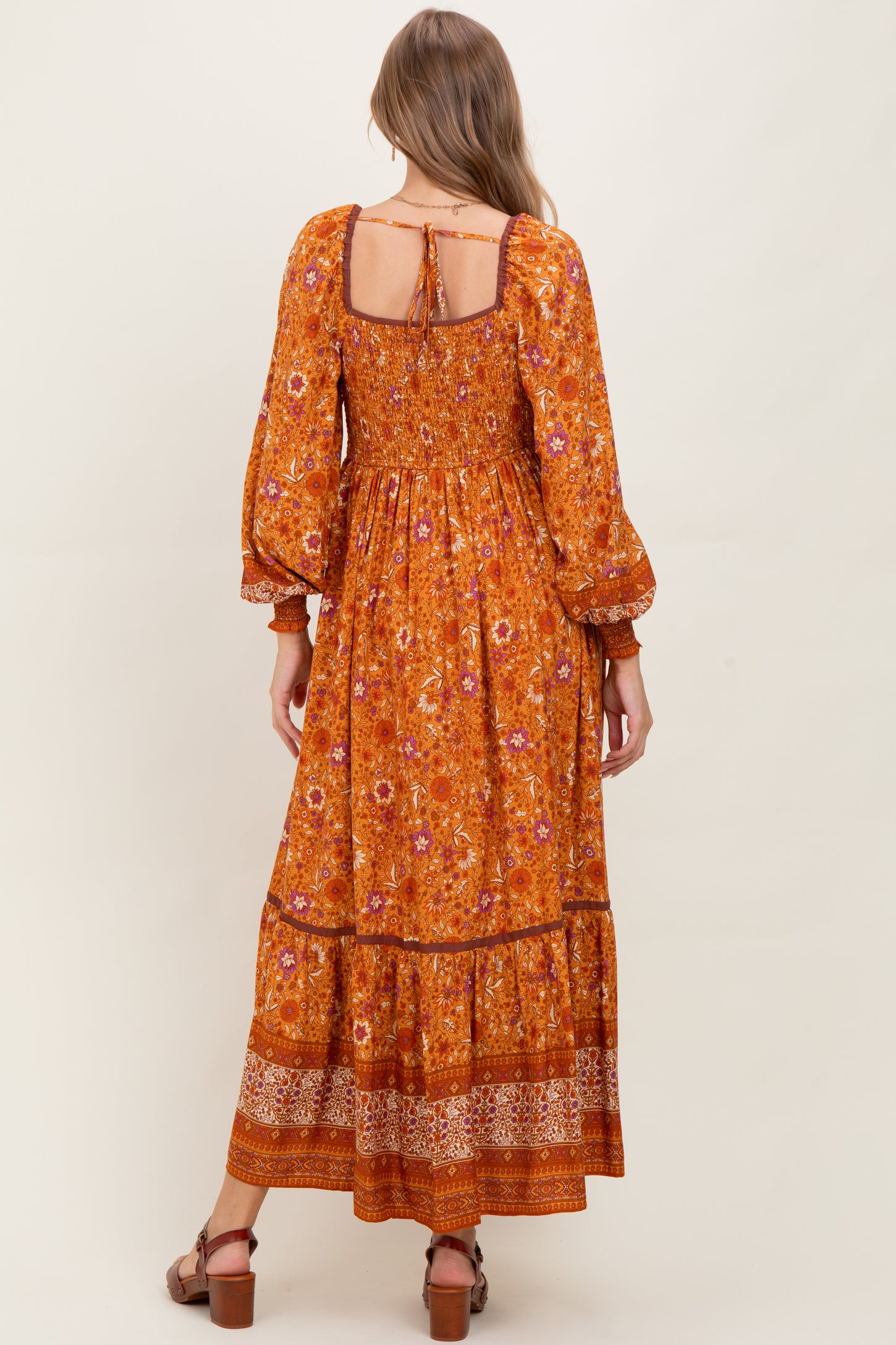 woman wearing an orange floral maternity dress with puffed sleeves and a tiered skirt, showing a baby bump from the back