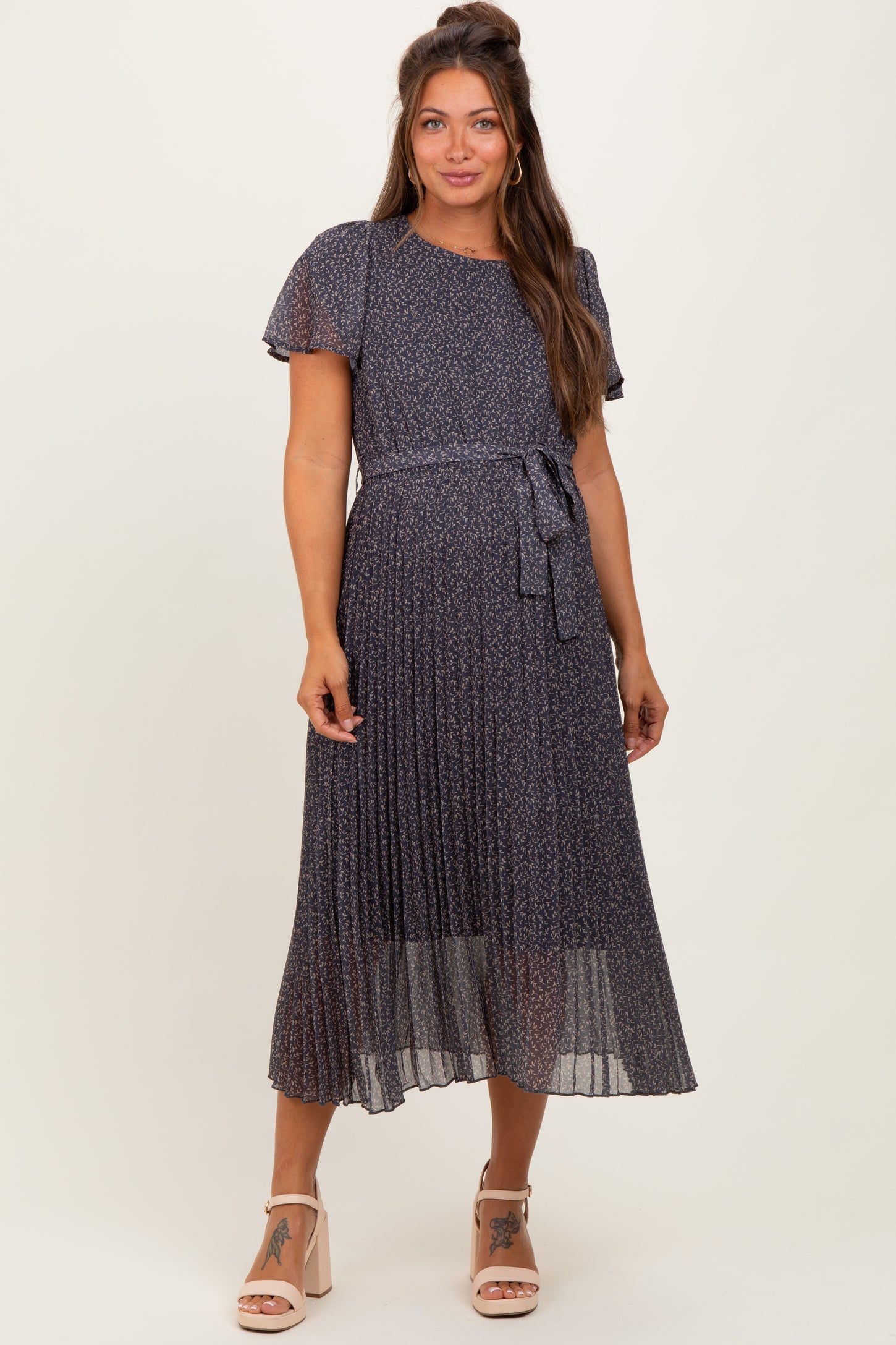 woman wearing a navy floral pleated maternity dress with short sleeves and a tied waist detail
